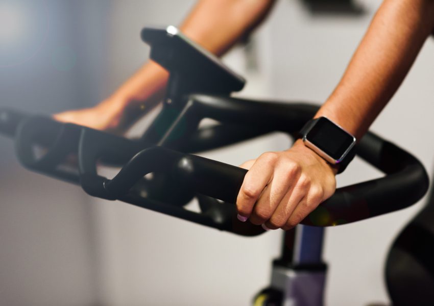 Hands of a woman training at a gym doing spinning or cyclo indoor with smart watch. Sports and fitness concept.